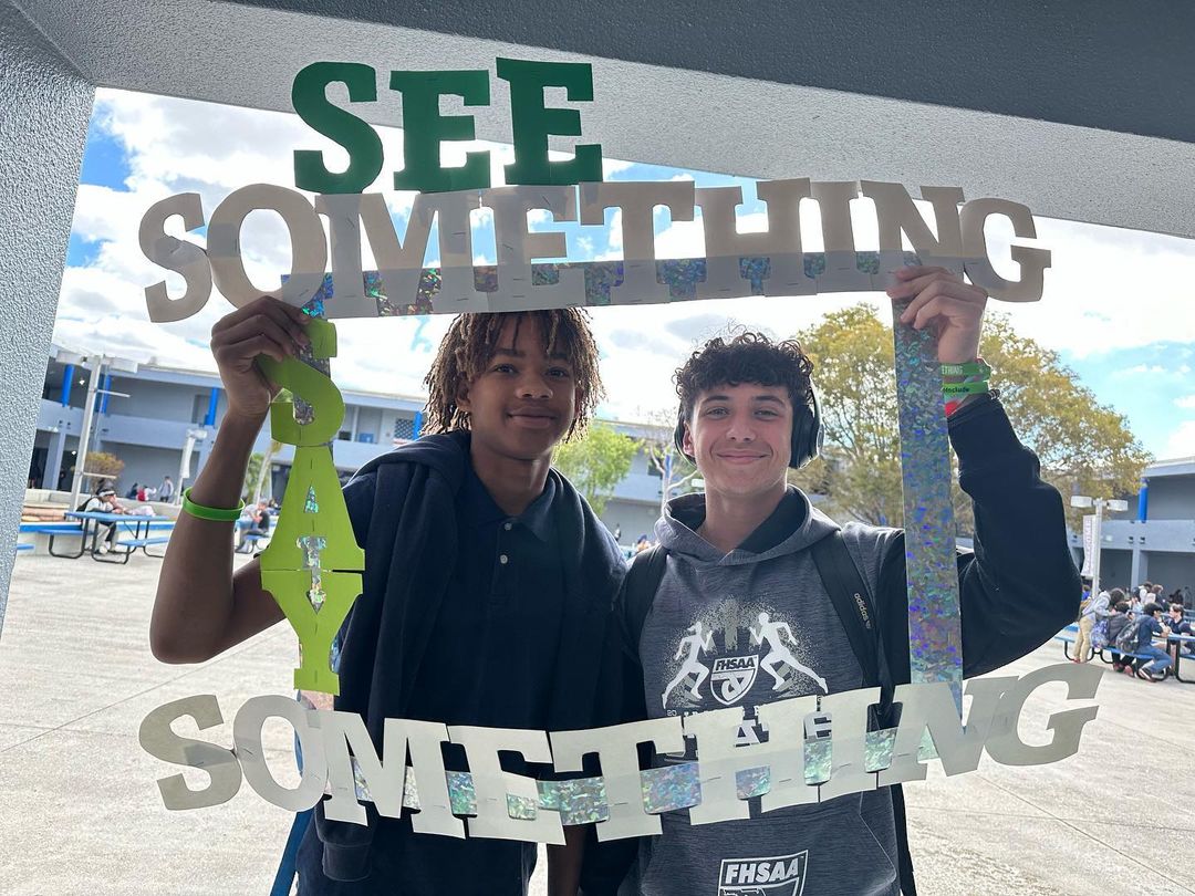 Two students smiling holding frame around themselves with See Something text